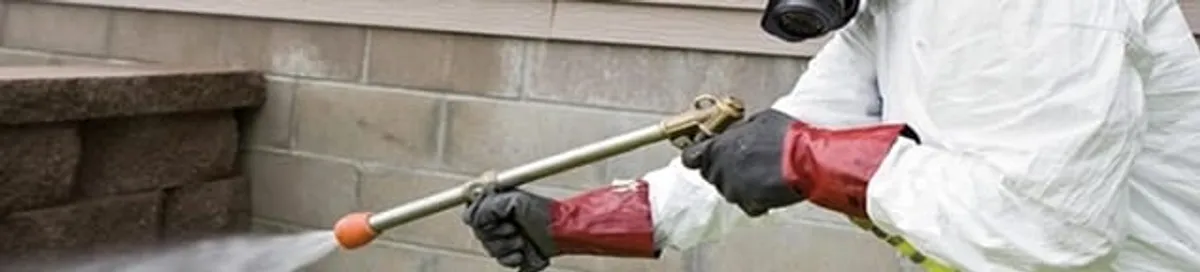Pest control technician applying exterior insect treatment along a home foundation in Nashua, NH