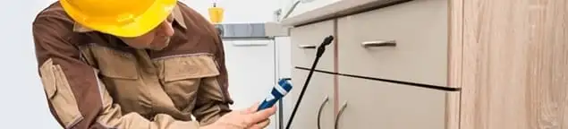 Roach exterminator applying treatment under kitchen cabinets in Nashua, NH