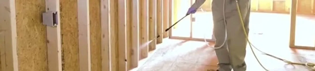 Termite treatment technician applying spray along framing and unfinished walls in Nashua, NH